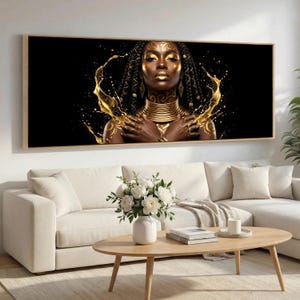 May include: A framed art print depicting a woman adorned with gold body paint and jewellery set against a black backdrop. Gold liquid splashes surround her. The artwork hangs above a white sofa and a wooden coffee table with a vase of white flowers.