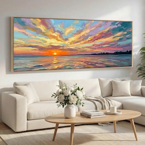 May include: A large rectangular oil painting of a sunset over the sea. The sky is filled with vibrant colours of orange, yellow, pink, and blue. The artwork is framed in a light-coloured wooden frame and hangs above a white sofa.