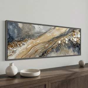 May include: Abstract art print in a gray wooden frame. The artwork features a flowing design with shades of gold, beige, and gray, accented with gold leaf and black lines. The piece has a modern, elegant aesthetic, suitable for home decor.
