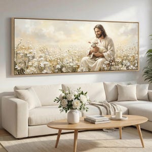 Op de afbeelding: Een ingelijste canvas kunstdruk toont een serene scène van een figuur die een lam vasthoudt in een veld met witte bloemen. Het kunstwerk maakt gebruik van zachte, neutrale tinten en wordt weergegeven boven een witte bank en een houten salontafel.
