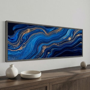 May include: A rectangular wall art piece featuring a fluid abstract design with swirling shades of deep navy and royal blue, accented by metallic gold veins that flow horizontally across the canvas, enclosed in a dark gray frame.