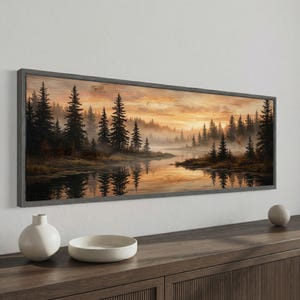 May include: A framed landscape art print depicts a serene forest scene with a river reflecting the trees and a golden sunset. The artwork is encased in a gray wooden frame, creating a rustic aesthetic. The print showcases a tranquil natural environment.