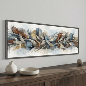 May include: A panoramic framed wall art piece featuring abstract graffiti-style lettering in shades of brown, blue, and grey. The composition includes sharp, angular lines, layered shapes, and paint drip effects on a light, neutral background.