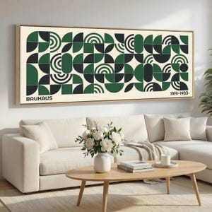 May include: A framed Bauhaus art print featuring a geometric design in shades of green, black, and white. The artwork includes the word "BAUHAUS" and the dates "1919-1933". The print is displayed above a white sofa and wooden coffee table.