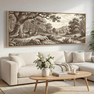 May include: A sepia-toned framed artwork depicts a serene forest scene with two deer resting under a large tree. The detailed illustration showcases a river, trees, and a distant landscape, creating a tranquil ambiance. The artwork is displayed above a white sofa.