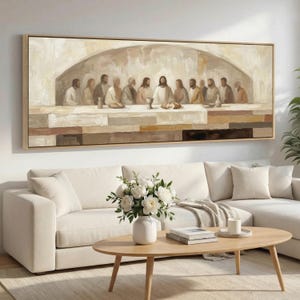 May include: A framed rectangular canvas art piece depicting the Last Supper. The painting features a neutral colour palette with figures seated around a table. The artwork is displayed above a white sofa and a wooden coffee table.