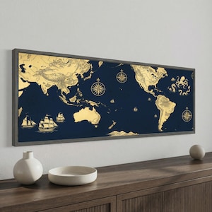 May include: A rectangular wall art piece featuring a world map in gold on a dark navy blue background. The map includes illustrations of sailing ships, a compass rose, and a sea creature. The entire artwork is enclosed in a dark gray frame.