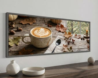 May include: A panoramic framed wall art print featuring a speckled ceramic mug filled with latte art, a black spoon on a white napkin, scattered dried autumn leaves, small berries, and a lit candle on a rustic wooden table surface.