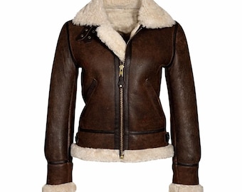 May include: A dark brown leather jacket featuring a thick cream-colored shearling lining, a wide fold-over collar, and long sleeves with shearling cuffs. The jacket includes a central gold-tone metal zipper, two side pockets, and adjustable side straps.