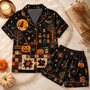 May include: A black short-sleeve pajama set featuring a Halloween print with a haunted house, jack-o'-lanterns, black cats, bats, and a witch silhouette against a full moon. The design includes a patchwork quilt pattern at the hem and orange piping.