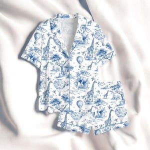 Puede incluir: Conjunto de pijama blanco y azul con estampado toile de Jouy de tem&aacute;tica safari. La parte superior de manga corta y los pantalones cortos muestran jirafas, elefantes, globos aerost&aacute;ticos y &aacute;rboles. Camisa con botones y ribete blanco.