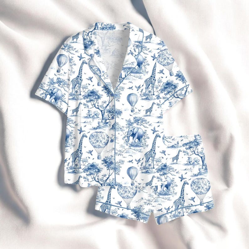 Puede incluir: Conjunto de pijama blanco y azul con estampado toile de Jouy de tem&aacute;tica safari. La parte superior de manga corta y los pantalones cortos muestran jirafas, elefantes, globos aerost&aacute;ticos y &aacute;rboles. Camisa con botones y ribete blanco.