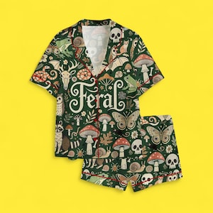 May include: Green pajama set with a whimsical forest pattern featuring mushrooms, butterflies, skulls, and the word "Feral". The set includes a short-sleeved button-up shirt and matching shorts, both trimmed with red piping.