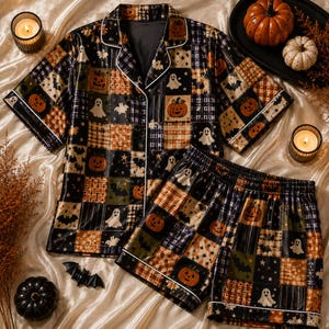 May include: A short-sleeve button-down pajama shirt and matching shorts set featuring a patchwork pattern of orange pumpkins, white ghosts, black bats, and stars on a dark background with white piping trim along the edges and collar.