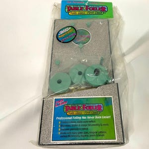 May include: A Table Foiler kit for glass foiling, packaged in clear plastic. The kit includes a grey work surface, green foil rolls, and the text "Table Foiler Foils Glass - First Class". The kit also includes the text "Professional Foiling Has Never Been Easier!"