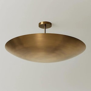 May include: A large, brass-coloured ceiling light fitting. The light has a wide, shallow bowl shape and a central stem attached to a circular ceiling mount. The fitting is made of metal and has a warm, metallic finish.