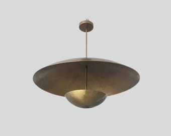 Może przedstawiać: Mosiężna lampa wisząca w stylu mid-century modern. Lampa posiada duży, płaski, tarczowaty klosz nad mniejszym, miseczkowatym kloszem. Oprawa zwisa z centralnego pręta i okrągłego mocowania sufitowego.