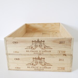 Op de afbeelding: Twee houten wijnkisten op elkaar gestapeld. De kisten zijn gelabeld met de tekst "Blason d'Issan Margaux" en het jaar "2011". De kisten zijn ook gelabeld met de tekst "CRD" en "6 Billes".