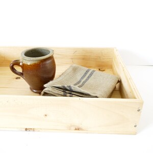 Op de afbeelding: Een houten dienblad met een bruine keramische mok en een beige linnen theedoek met zwarte strepen.