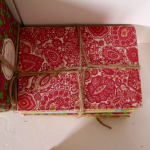 Puede incluir: Una pila de libros envueltos en papel estampado rojo y verde con cuerda marr&oacute;n. Los libros est&aacute;n atados con un lazo.