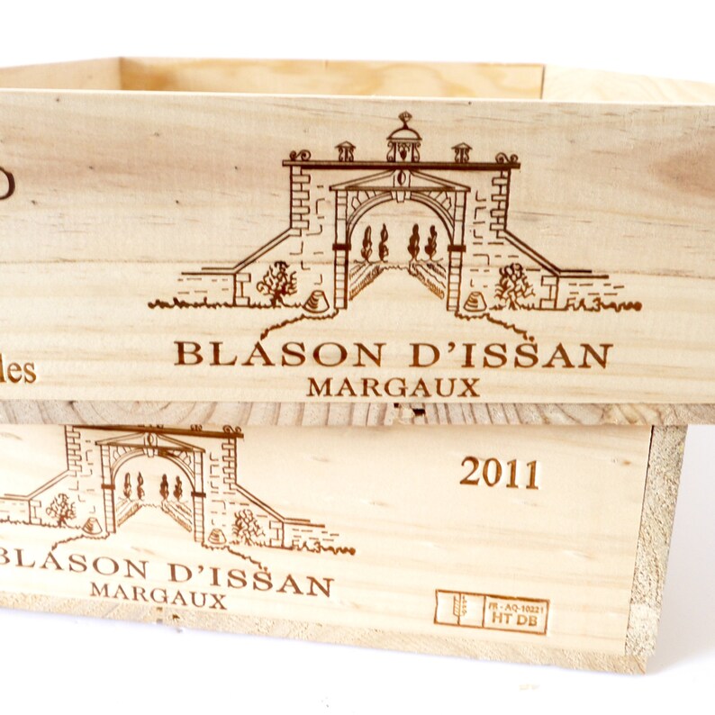 Op de afbeelding: Een houten wijnkist met de woorden "Blason d'Issan Margaux" en het jaar "2011" erop gedrukt. De kist heeft een tekening van een poort met een toren erop.