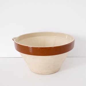 May include: A white ceramic mixing bowl with a brown rim. The bowl is slightly flared at the top and has a pour spout on one side.