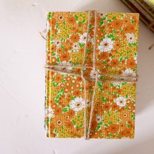Puede incluir: Una pila de libros antiguos de tapa dura con un patr&oacute;n floral en tonos naranja, amarillo y verde. Los libros est&aacute;n atados con cuerda.
