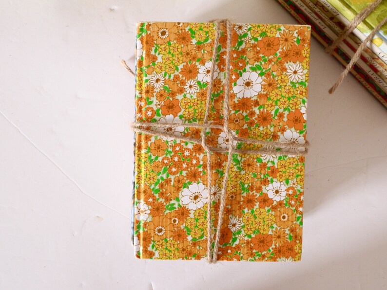 Puede incluir: Una pila de libros antiguos de tapa dura con un patr&oacute;n floral en tonos naranja, amarillo y verde. Los libros est&aacute;n atados con cuerda.