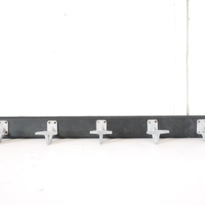 May include: A black wooden coat rack with five silver metal hooks. The hooks are shaped like a stylized letter 'T' and are attached to the front of the rack.