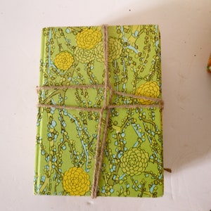 Puede incluir: Un libro verde y amarillo con un patr&oacute;n floral est&aacute; envuelto con cuerda. El libro est&aacute; atado con cuerda en un patr&oacute;n de cruz.