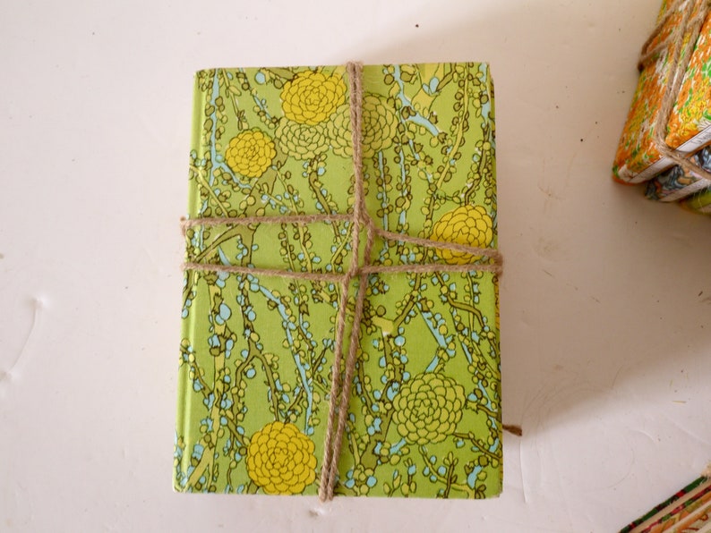 Puede incluir: Un libro verde y amarillo con un patr&oacute;n floral est&aacute; envuelto con cuerda. El libro est&aacute; atado con cuerda en un patr&oacute;n de cruz.
