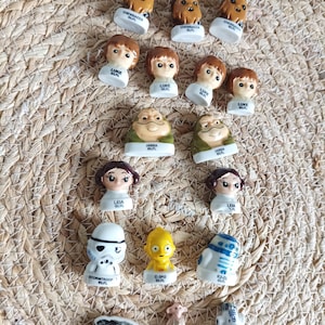 Puede incluir: Una colección de pequeñas figuras de personajes de Star Wars que incluye a Chewbacca, Luke, Jabba, Leia, Stormtrooper, C-3PO, R2-D2 y el Halcón Milenario. Cada pieza tiene una base blanca con el nombre y ©LFL impresos en negro.