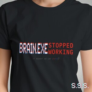 Może przedstawiać: Czarna koszulka z napisem "BRAIN.EXE STOPPED WORKING" z efektem glitch. Poniżej znajduje się "// REBOOT OR CRY (Y/N)?" w kolorze białym. Litery "S.S.S." są w prawym dolnym rogu.