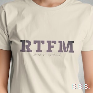 Könnte beinhalten: Cremefarbenes T-Shirt mit den Buchstaben "RTFM" in einem schattierten, lila Farbton. Darunter steht der Text "Read the f***ing Manual". Das Shirt hat auch die Buchstaben "S.S.S." in einem Glitch-Effekt.
