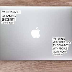 Puede incluir: Dos pegatinas blancas con texto negro en un portátil plateado. La pegatina superior dice "Soy incapaz de fingir sinceridad. - Stevie Budd". La pegatina inferior dice "Estoy intentando muy duro no conectar con la gente ahora mismo. - David Rose".
