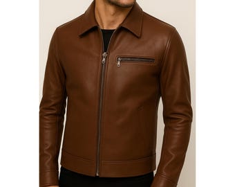 May include: A brown leather jacket with a collared neckline and a front zipper closure. The jacket features a small zippered pocket on the chest and two side pockets. The sleeves are long and fitted.