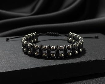May include: A black and silver beaded bracelet. The bracelet features two rows of black rectangular beads and silver spherical beads. The bracelet is on a black surface with a black background.