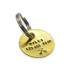 May include: Gold-coloured metal dog tag with the name "MYLES" and phone number "123 456 7890" engraved on the front. The tag has a split ring attached.