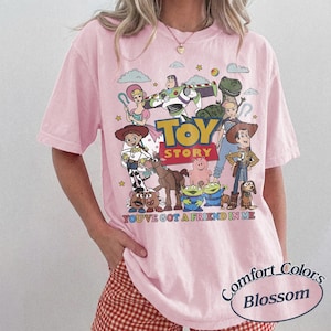 以下が含まれることがあります： ピンク色のComfort Colors Tシャツ。鮮やかなトイ・ストーリーのキャラクターのグラフィックが特徴です。 ウッディ、バズ・ライトイヤー、その他の映画のキャラクターがデザインされており、「TOY STORY」と「YOU'VE GOT A FRIEND IN ME」の文字が入っています。