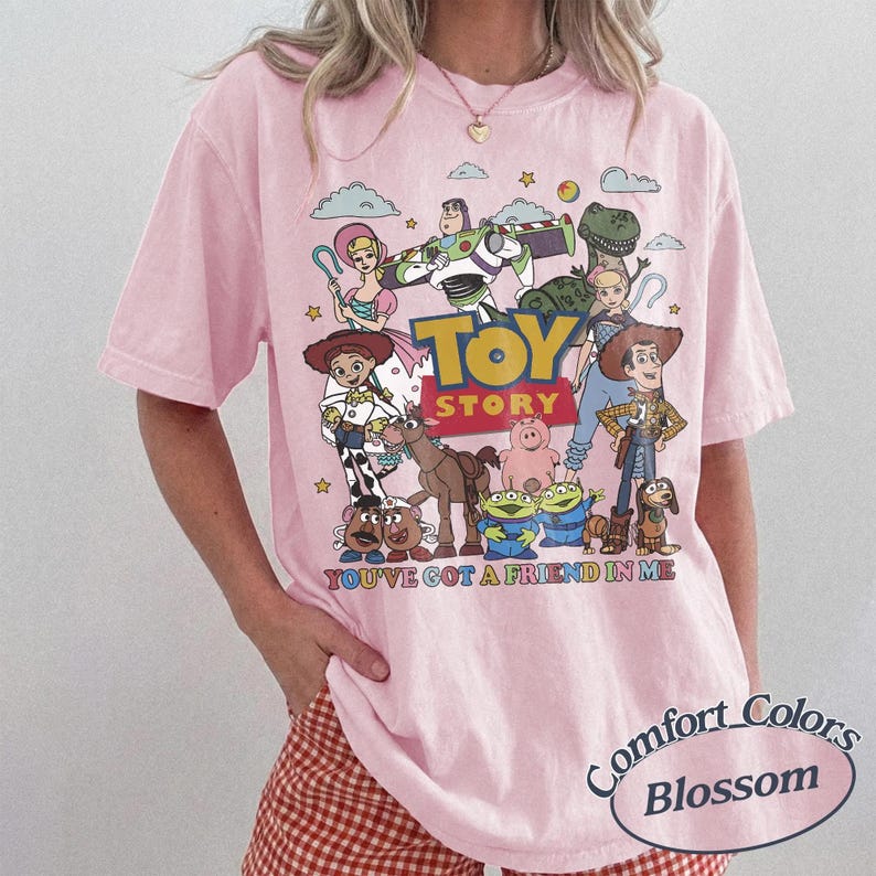 以下が含まれることがあります： ピンク色のComfort Colors Tシャツ。鮮やかなトイ・ストーリーのキャラクターのグラフィックが特徴です。 ウッディ、バズ・ライトイヤー、その他の映画のキャラクターがデザインされており、「TOY STORY」と「YOU'VE GOT A FRIEND IN ME」の文字が入っています。