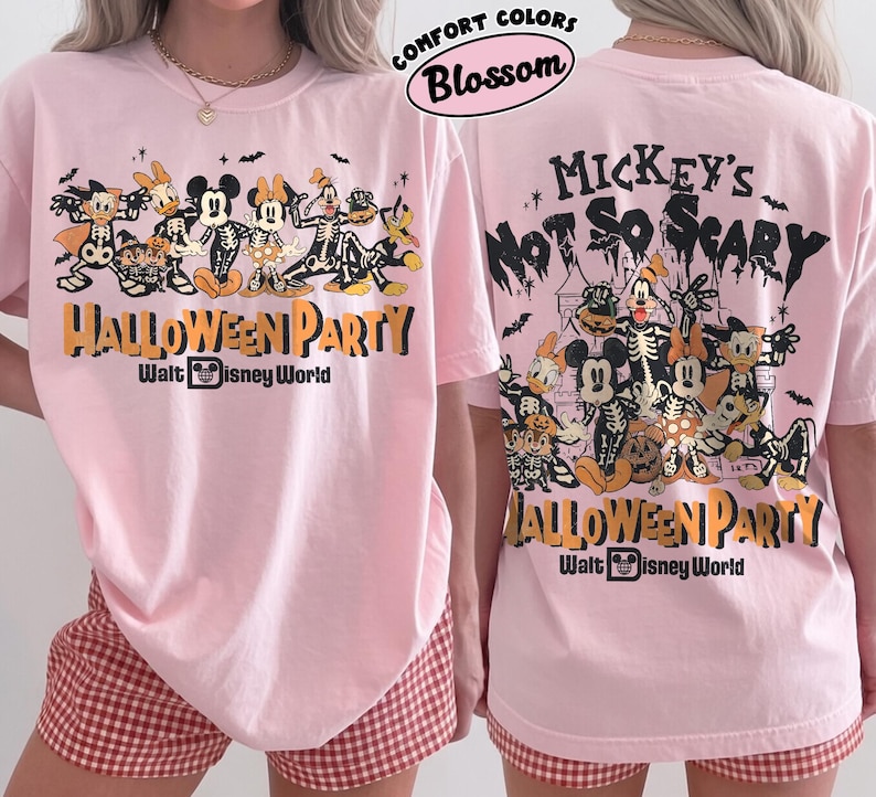 May include: A light pink t-shirt featuring a graphic of Disney characters in skeleton costumes. The front displays the text Halloween Party Walt Disney World. The back shows the same characters with the text Mickey's Not So Scary Halloween Party Walt Disney World. The shirt is labeled Comfort Colors Blossom.