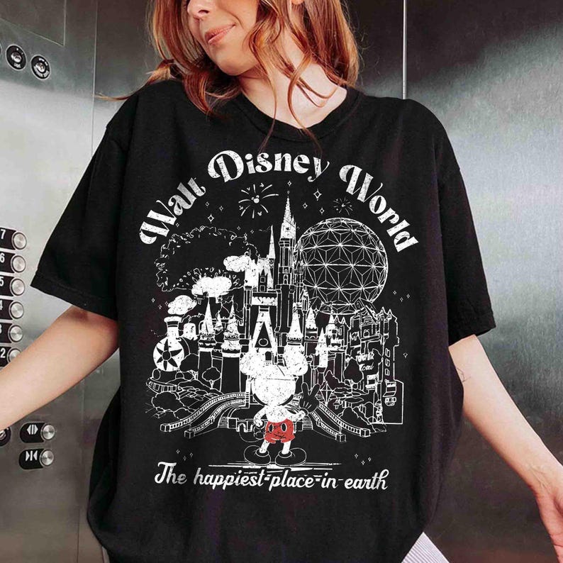 May include: Black t-shirt featuring a white graphic of Walt Disney World with Mickey Mouse. The design includes a castle, Spaceship Earth, and the text "The happiest place on earth."