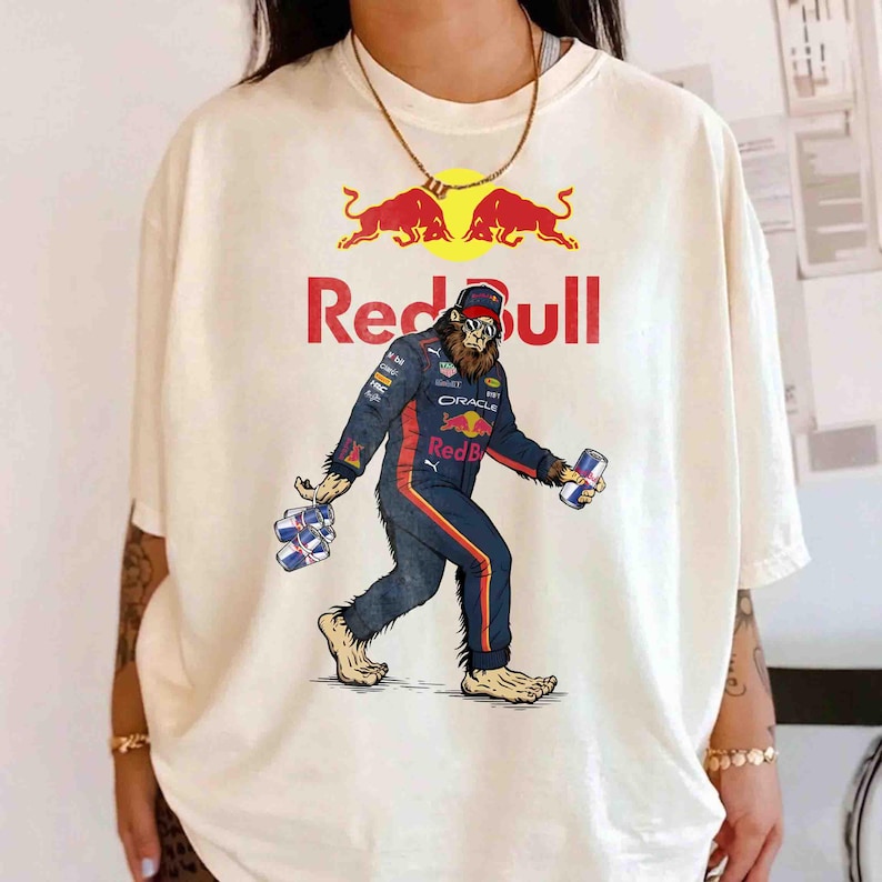 Pu&ograve; includere: T-shirt color crema con una figura simile a Bigfoot in tuta da corsa Red Bull, che tiene in mano lattine di energy drink. Il logo e il testo Red Bull sono sopra la figura. Il design include un sole giallo e due tori rossi.