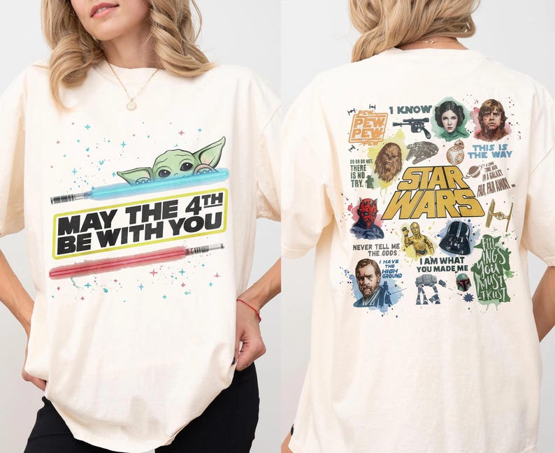 May include: Cream-colored t-shirt featuring a graphic of Baby Yoda with a blue lightsaber and a red lightsaber. The text "MAY THE 4TH BE WITH YOU" is printed below. The back of the shirt has Star Wars characters and quotes.