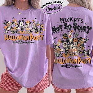 May include: A light purple t-shirt featuring a graphic of Disney characters in skeleton costumes. The front and back display the text Mickey's Not So Scary Halloween Party Walt Disney World with illustrations of Mickey, Minnie, Donald, and Goofy.