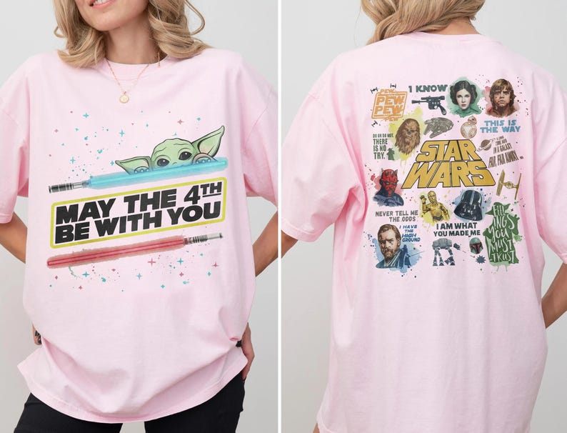 May include: A light pink Star Wars t-shirt. The front features Baby Yoda, a blue lightsaber, a red lightsaber, and the text "MAY THE 4TH BE WITH YOU." The back has various Star Wars characters and quotes.