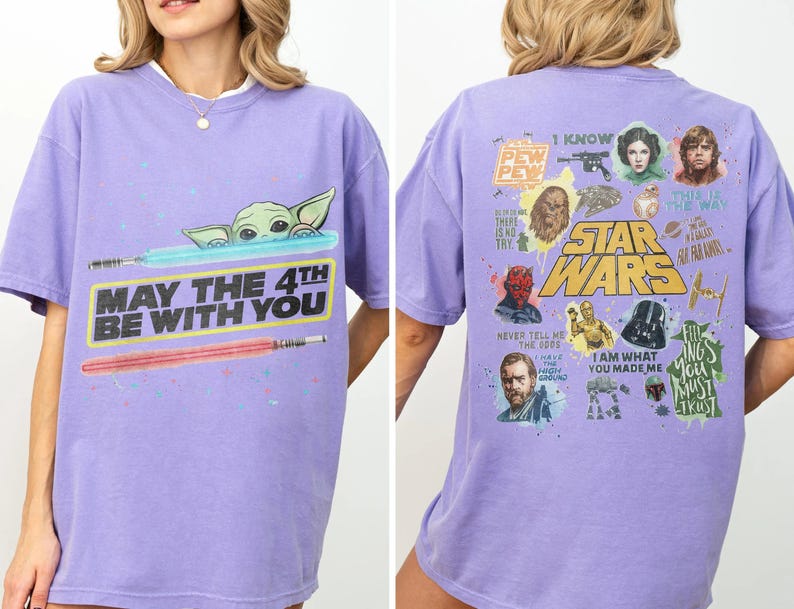 May include: A lilac-colored t-shirt featuring a Star Wars theme. The front displays Baby Yoda with lightsabers and the text "MAY THE 4TH BE WITH YOU." The back showcases various characters and phrases from the Star Wars saga.