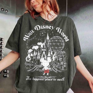 May include: Dark green t-shirt with a white graphic of the Walt Disney World logo, including a castle, Spaceship Earth, and Mickey Mouse. The text "Walt Disney World" and "The happiest place on earth" are also printed on the shirt.