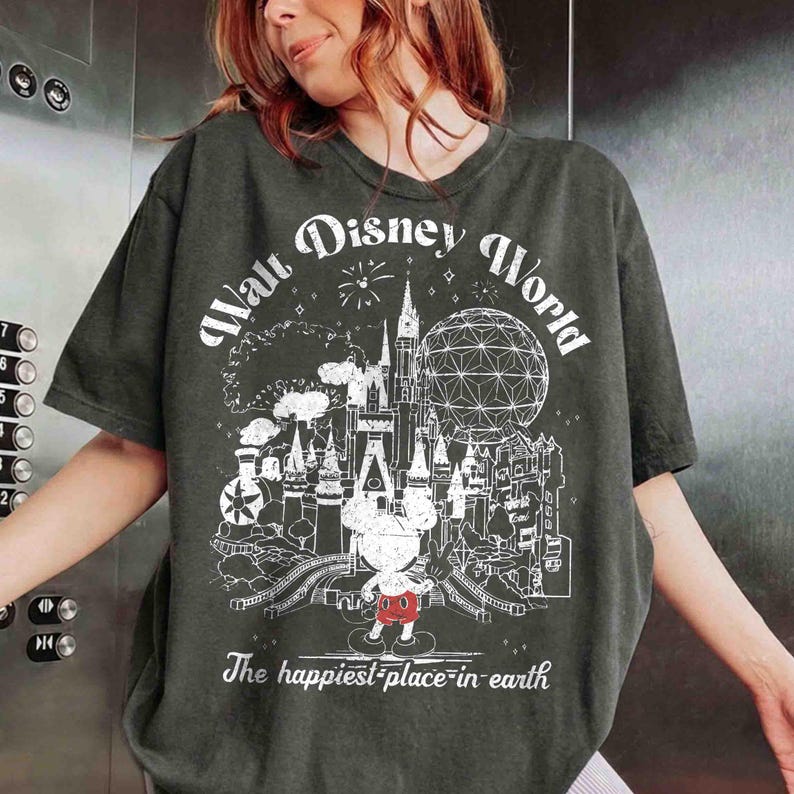 May include: Dark green t-shirt with a white graphic of the Walt Disney World logo, including a castle, Spaceship Earth, and Mickey Mouse. The text "Walt Disney World" and "The happiest place on earth" are also printed on the shirt.