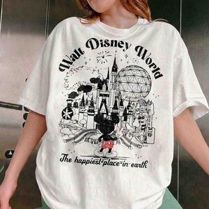 May include: White t-shirt with a black and white graphic of Walt Disney World. The design includes a castle, Spaceship Earth, Mickey Mouse, and the text "Walt Disney World" and "The happiest place on earth."